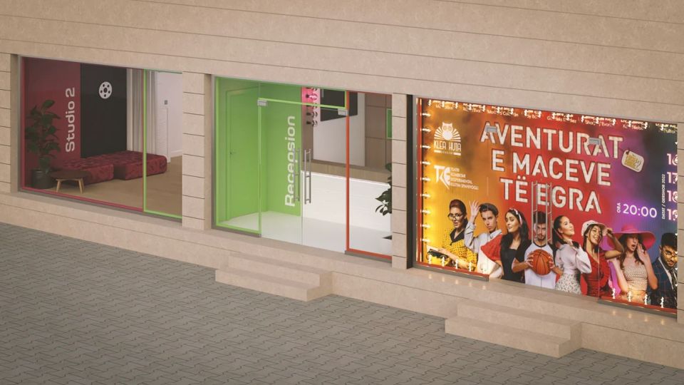 Street-level view of a modern building facade with large glass storefront windows and color-accented frames, including entrances labeled “Studio 2” and “Renaissance.” A brightly lit event poster fills one window, and shallow steps lead up from a paved sidewalk.